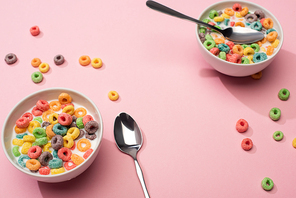 selective focus of bright colorful breakfast cereal with milk in bowls with spoons on pink background