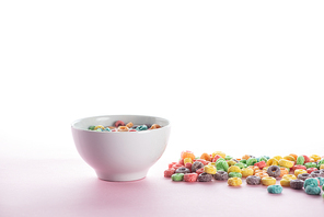 bright multicolored breakfast cereal scattered around bowl on white background