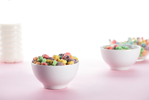 selective focus of bright multicolored breakfast cereal in bowls near milk on white background