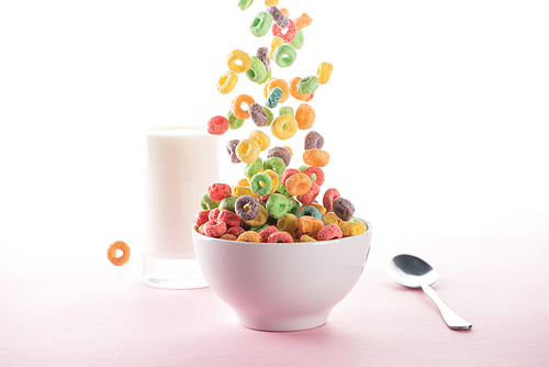 selective focus of bright multicolored breakfast cereal falling in bowl near milk and spoon on white background