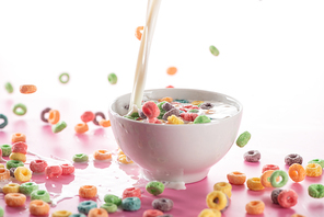 bright multicolored breakfast cereal in bowl with pouring milk on pink background