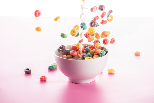 bright multicolored breakfast cereal in bowl with milk splash on pink background