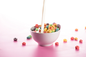 bright multicolored breakfast cereal in bowl with pouring milk on pink background