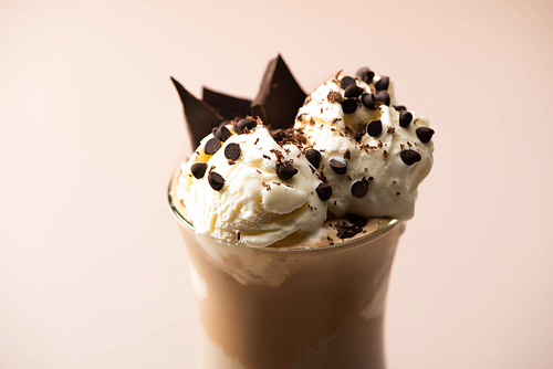 Glass of milkshake with ice cream, pieces of chocolate and candies on beige background
