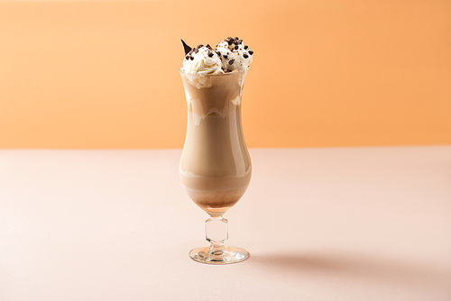 Glass of milkshake with ice cream and chocolate morsels on beige and orange