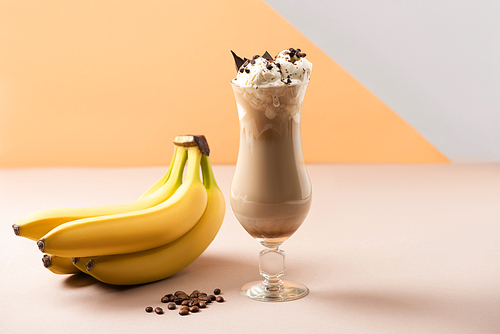 Glass of milkshake with chocolate morsels near bananas and coffee grains on beige, grey and orange