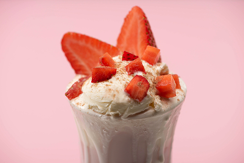 Selective focus of glass of milkshake with ice cream and cut strawberries isolated on pink