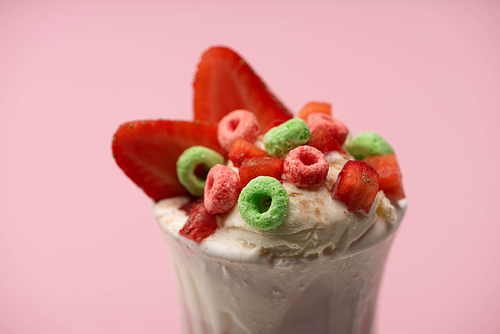 Selective focus of glass of milkshake with ice cream, cut strawberries and candies isolated on pink