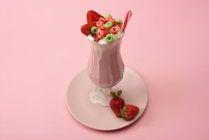high angle view of glass of milkshake with  straw, candies and strawberries on plate on pink background