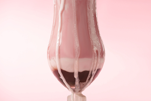 Glass of strawberry milkshake with ice cream dripping on pink background