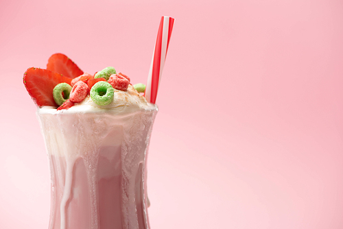 glass of milkshake with ice cream, colorful candies, strawberry halves and  tube on pink background