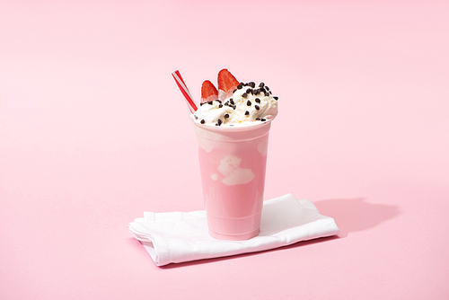 disposable cup of milkshake with  straw, chocolate chips and strawberry halves on napkins on pink