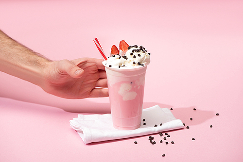 Cropped view of male hand with disposable cup of milkshake with chocolate morsels and strawberry on napkins on pink