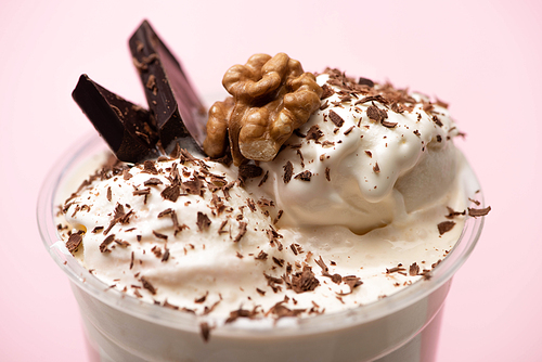 Disposable cup of milkshake with ice cream, walnut, chocolate shavings and pieces on pink background
