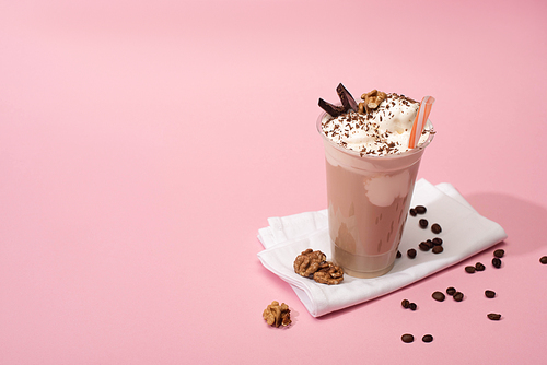 High angle view of disposable cup of chocolate milkshake with walnuts and coffee grains on napkins on pink