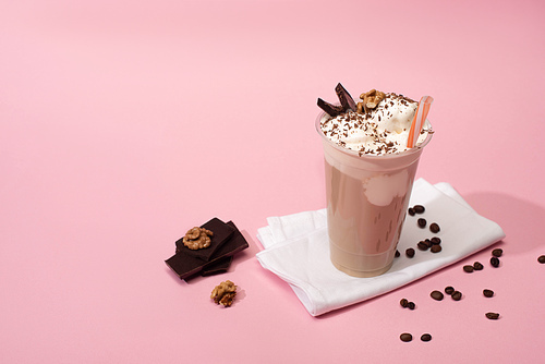 High angle view of disposable cup of milkshake with walnuts, chocolate pieces and coffee grains on napkins on pink