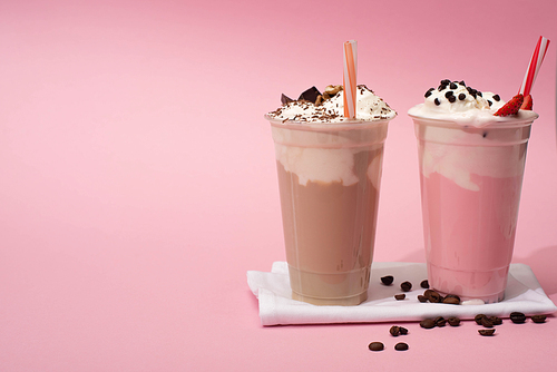 disposable cups of chocolate and strawberry milkshakes with  straws and coffee grains on napkins on pink