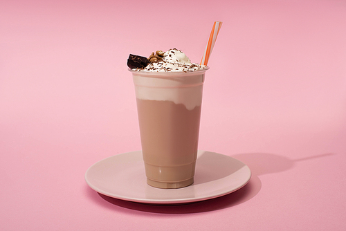 disposable cup of chocolate milkshake with  straw on plate on pink background