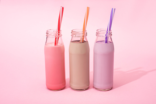 bottles of berry, strawberry and chocolate milkshakes with  straws on pink background