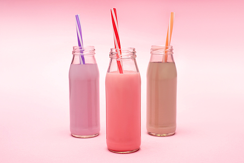 bottles of colorful berry, strawberry and chocolate milkshakes with  straws on pink