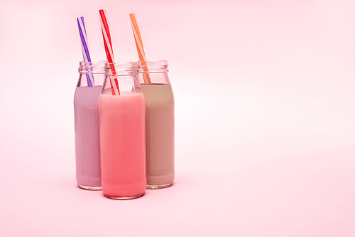 bottles of berry, strawberry and chocolate milkshakes with  straws on pink background