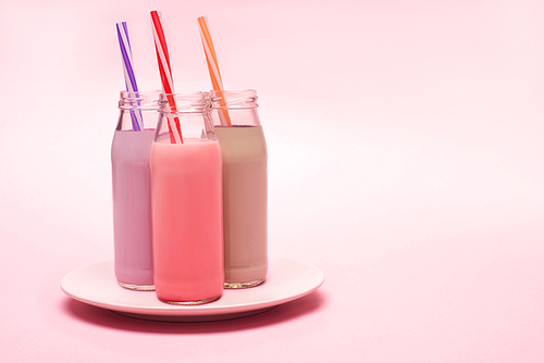 bottles of berry, strawberry and chocolate milkshakes with  straws on plate on pink background