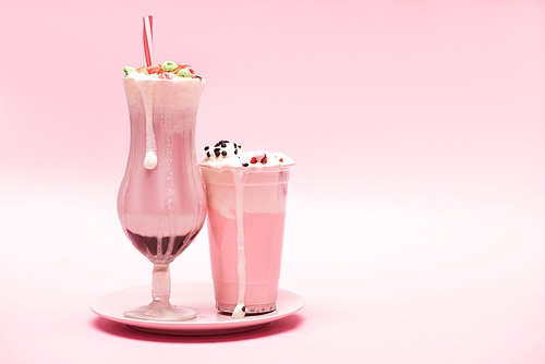 Disposable cup and glass of strawberry milkshakes on plate on pink background