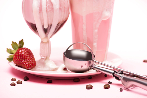 Disposable cup and glass of milkshakes, strawberry and scoop on plate with coffee grains on pink background