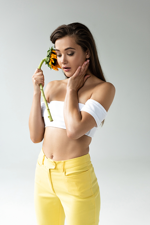 beautiful woman in yellow pants posing with sunflower isolated on grey