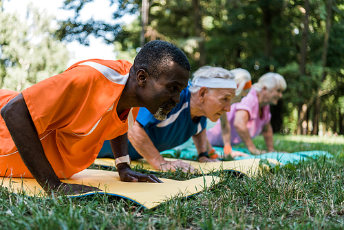 selective focus of african american man doing push ups with retired pensioners on fitness mats