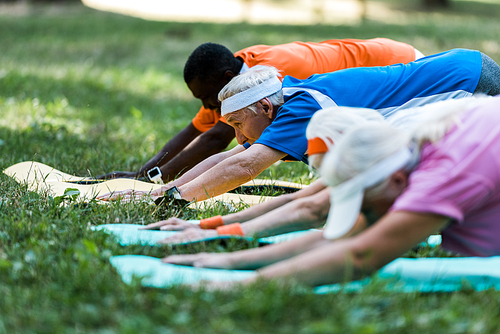selective focus of multicultural senior men and women stretching on fitness mats in park