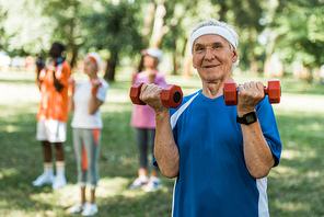 selective focus of happy senior man holding dumbbells in park