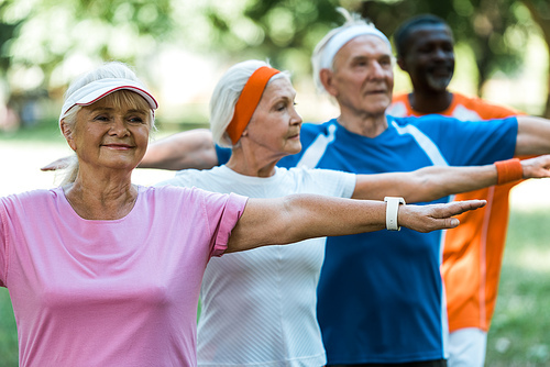 selective focus of happy retired woman standing with outstretched hands near multicultural pensioners