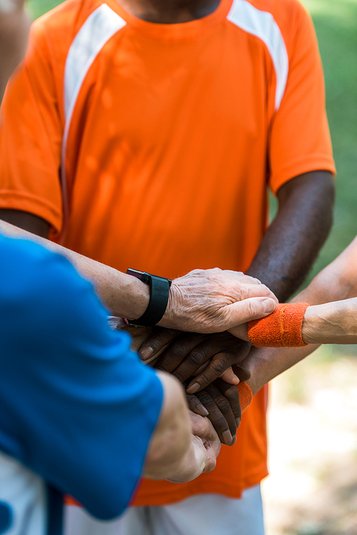 cropped view of multicultural retired men and women putting hands together