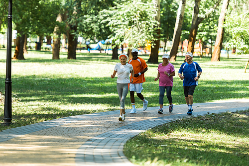 selective focus multicultural retired men and women in sportswear jogging in walkway in park