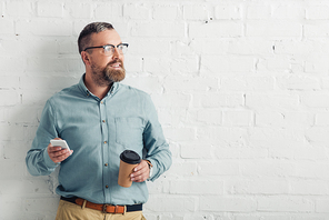 handsome businessman in shirt and glasses holding smartphone and paper cup