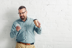 handsome businessman in shirt and glasses holding smartphone and paper cup