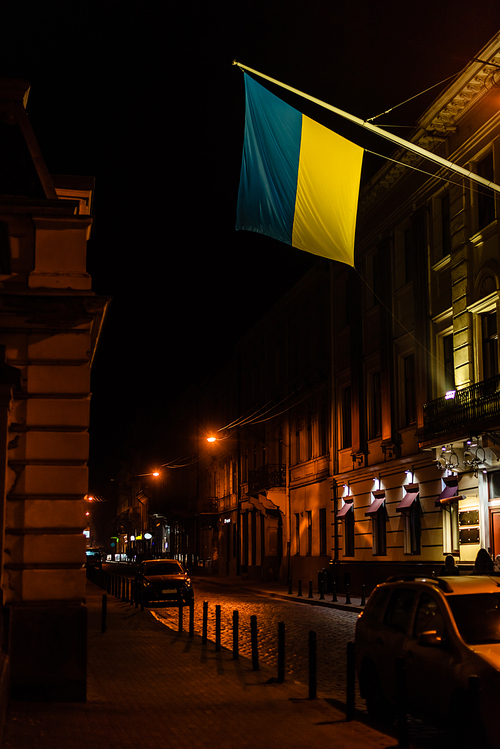cars parked on dark street near ukrainian flag