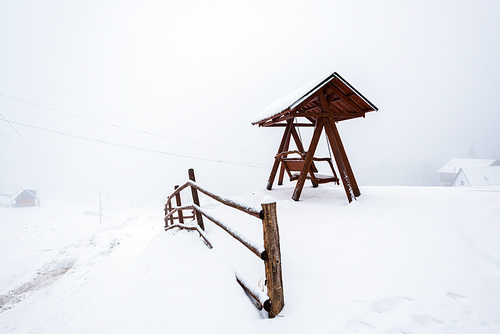 wooden fence and swing in snowy mountain village in fog