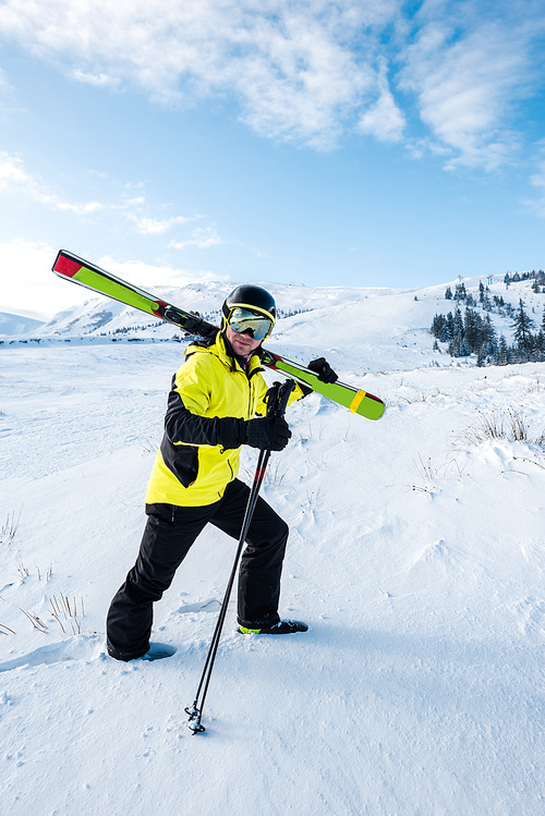 skier in helmet and goggles walking with sticks on white snow in mountains