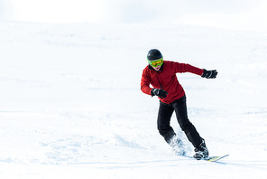 athletic snowboarder in helmet and goggles gesturing while riding on slope outside