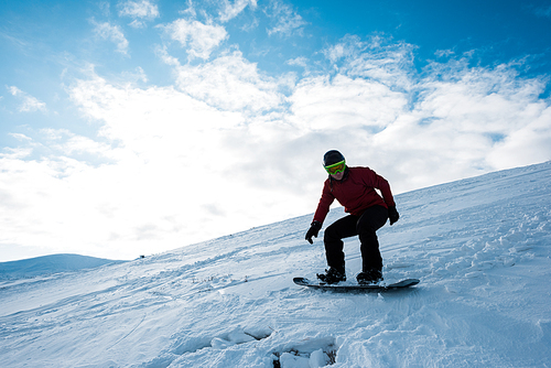 athletic snowboarder riding on slope against blue sky in winter
