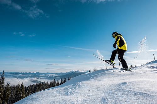 side view of skier holding ski sticks and making step against sky in mountains