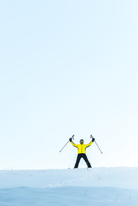 skier in helmet holding sticks while standing on snow in mountains