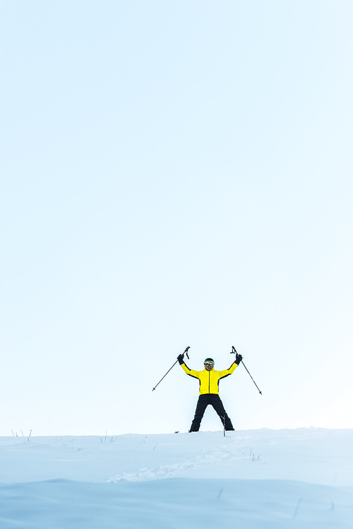 skier in helmet holding sticks while standing on snow in mountains