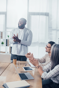 smiling multicultural colleagues clapping during meeting in creative agency