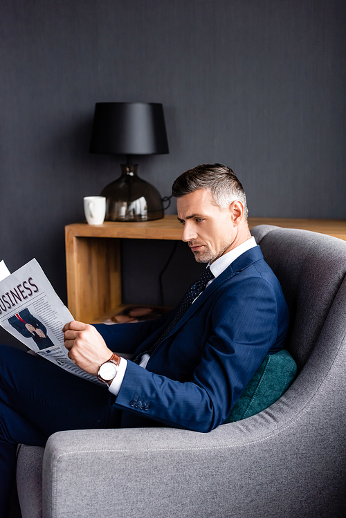 side view of businessman in suit reading newspaper with business lettering and sitting in armchair