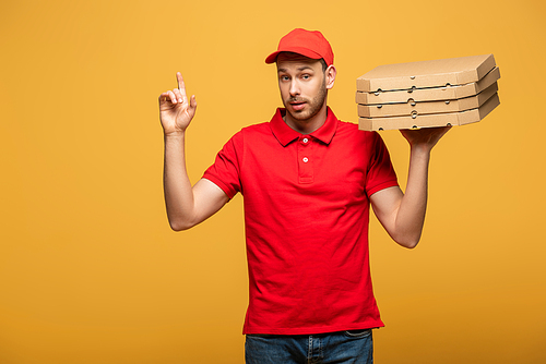 delivery man in red uniform holding pizza boxes and showing idea gesture isolated on yellow