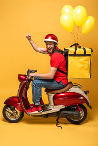side view of happy delivery man with balloons on backpack on scooter showing fist on yellow background