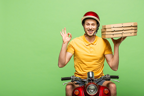 smiling delivery man in yellow uniform on scooter delivering pizza and showing ok sign isolated on green